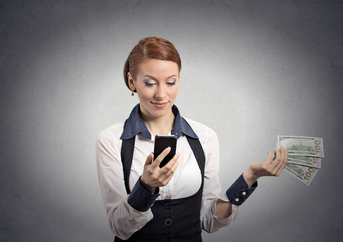 Woman looking at smart phone holding cash.